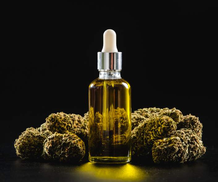 bottle of cbd oil with buds surrounding it in a black background